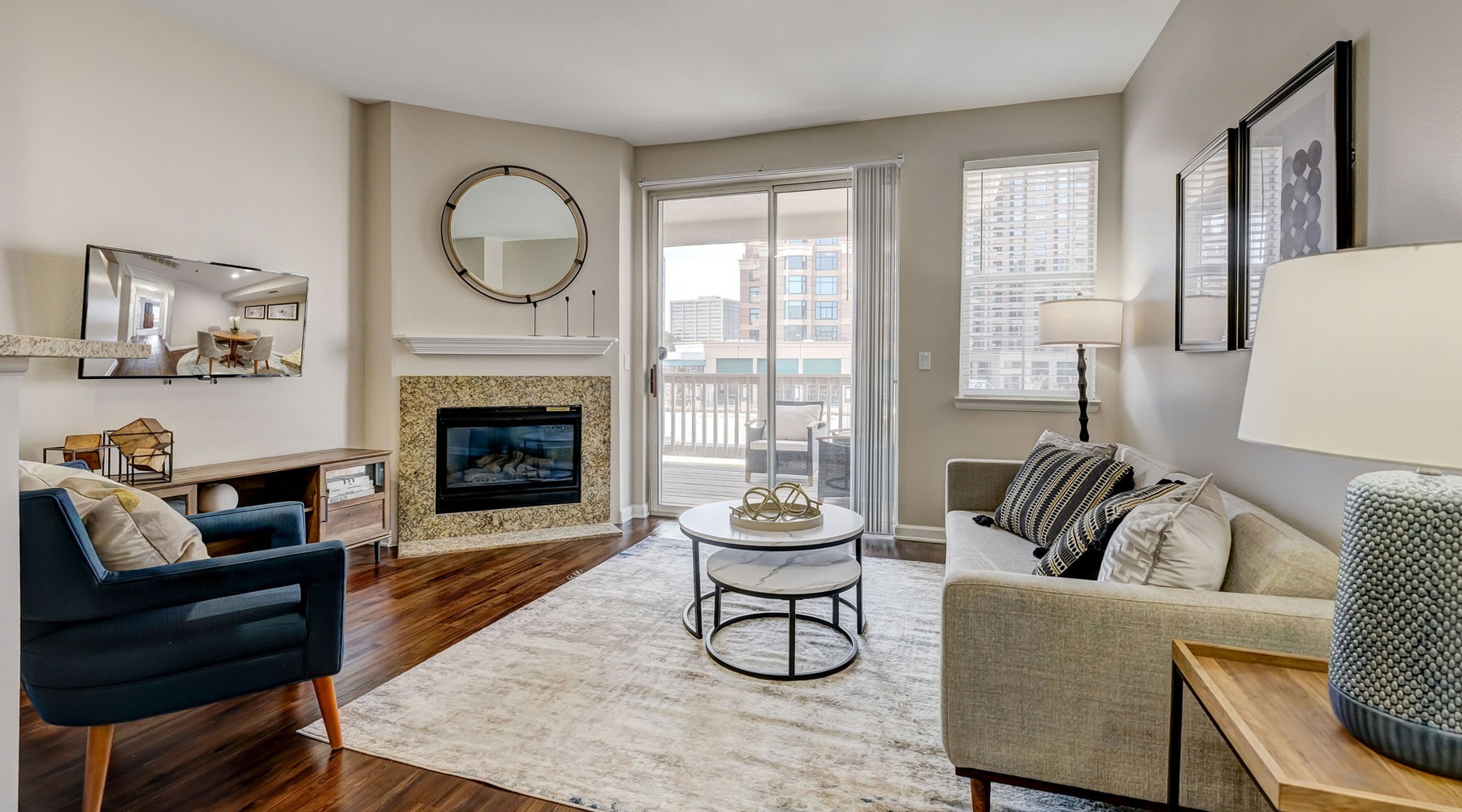 A cozy living room features a fireplace, a round mirror, a sofa with patterned pillows, and a dark armchair.